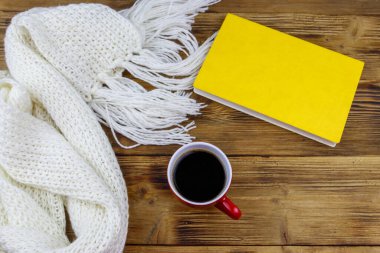 Ahşap masada örülmüş beyaz eşarp, kitap ve bir fincan kahve. Üst Manzara. Kış konsepti