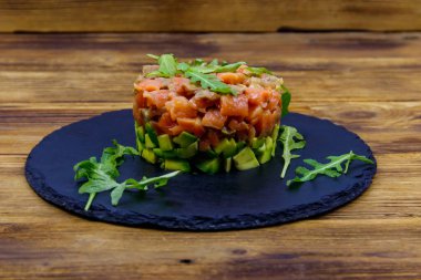 Avokado ve roka ile ahşap masada somon tartar.