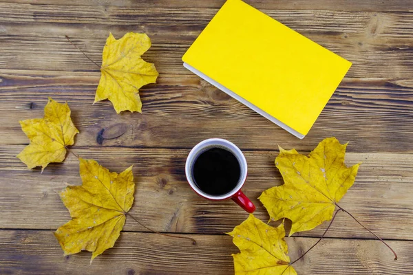 Cup of coffee, book and autumn maple leaves on wooden table. Top view. Autumn cozy concept