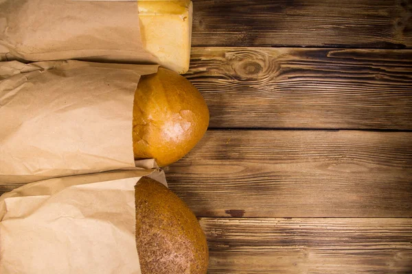 Assortment of bread packed in paper on wooden table. Top view, copy space