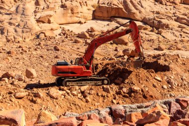 Orange excavator working at construction site in desert in Sinai peninsula, Egypt