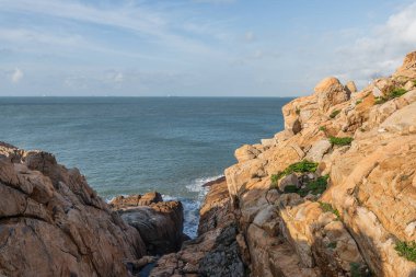 Mavi gökyüzünün altında deniz tarafından yıpranmış çeşitli şekillerde taşlar.