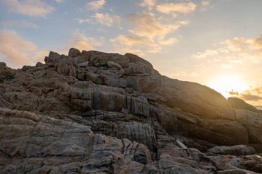 Sabah, güneş kayalıklarda parlar ve sahilde dalgalar.;