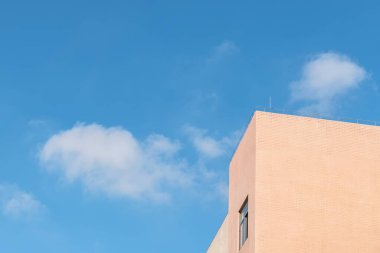 Mavi gökyüzünün ve beyaz bulutların altındaki açık sarı binanın bir parçası.