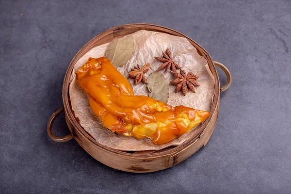 Stewed yellow pig feet in bamboo containers against a dark background