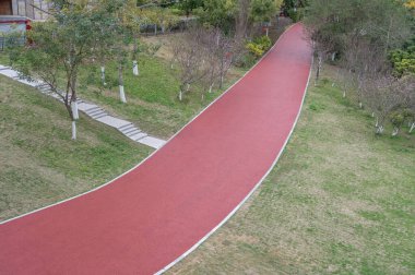 Modern şehir parkındaki kırmızı asfalt pist her iki taraftaki yeşil bitkilerle çevrilidir.
