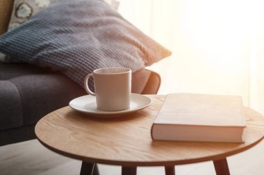 Evde rahatla, bir fincan sıcak çay ve kanepenin yanındaki sehpanın üzerinde kitap.