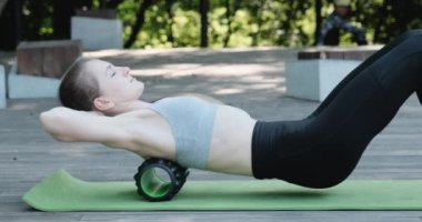 Yoga minderindeki genç bir kadın MFR silindiriyle sırt masajı yapıyor. Bağ ağrısı için masaj rulosu. Açık hava eğitimi. Yüksek kalite 4k görüntü