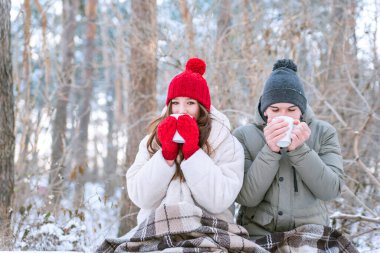 Aşıklar çay içerler ve kendilerini battaniyeye sararlar. Genç çift kışın parkta piknik yaptı.