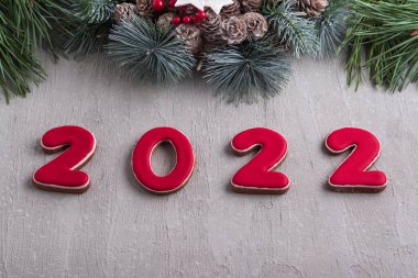 Kırmızı 2022 numara zencefilli çörek ve Noel çelengi. İyi yeni yıl ruhu. Arkaplanda açık gri duvar.