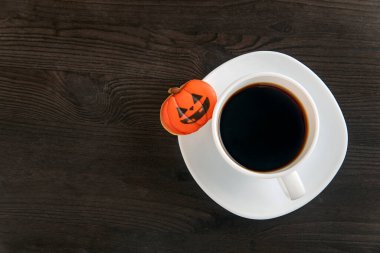 Cadılar Bayramı kahvesi masanın üstünde. Balkabağı şeklinde ilginç bir turuncu kurabiye beyaz bir tabağın üzerinde yatıyor. Uzayı kopyala Yüksek kalite fotoğraf