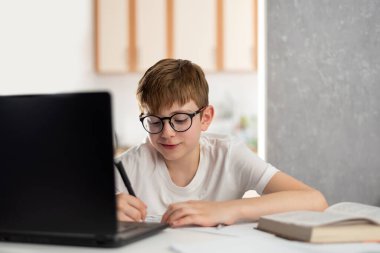 Uzaktan öğrenme sırasında çocuk evde dizüstü bilgisayarın yanında yazıyor. Online dersler. Genç çocuk bilgisayarda ödev yapıyor. Evde eğitim.