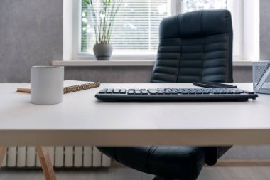 Rahat bir iş yeri. Deri ofis sandalyesi, bilgisayar klavyesi, defter ve kahve.