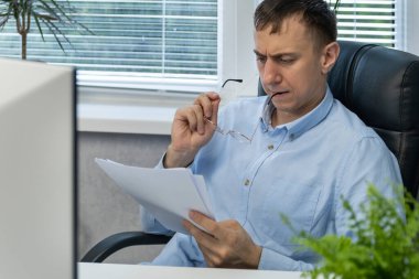 Odaklanmış ofis çalışanı belgeleri okur ve gözlük kemerini kemirir. Erkek muhasebeci. Yardımcı Yönetmen