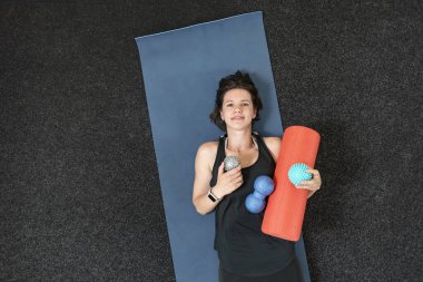 Genç atletik kız çeşitli miyofasyal rulolarla yoga minderinde yatıyor. MFR için ekipman. Miyofasyal tahliye. Üst görünüm.