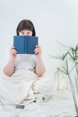 Elinde kitap olan genç bir kadının portresi. Kitaplı kız yatakta oturuyor. Dikey çerçeve