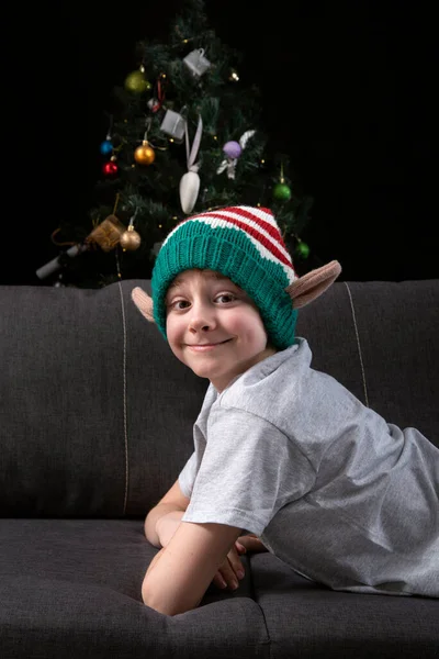 Szczęśliwy Uśmiechnięty Chłopak Kapeluszu Elfa Bożego Narodzenia Spoczywa Kanapie Patrzy — Zdjęcie stockowe