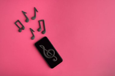 Akıllı telefon, üçlü anahtar ve pembe arka planda nota. Müzik uygulamaları. Telefonunda müzik var.
