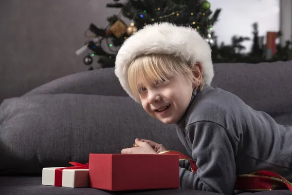 Мальчик Шляпе Санты Смотрит Свой Новогодний Подарок Лежащий Диване Фоне — стоковое фото