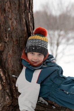 Kış manzarasında Bubo şapkalı neşeli çocuk portresi. Karla kaplı ormanda yürü