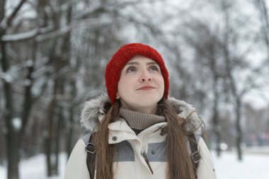 Kış parkında yürüyen kırmızı şapkalı genç kızın portresi. Kış ormanı geçmişinde güzel bir kadın