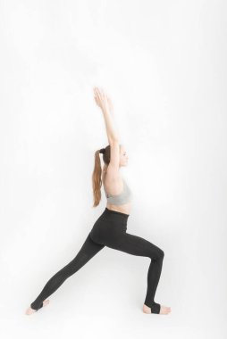 Virabhadrasana I. Savaşçı I Poz veriyor. Beyaz arka planda yoga yapan çekici bir kadın. Spor giyimli kız fitness yapıyor. Dikey çerçeve
