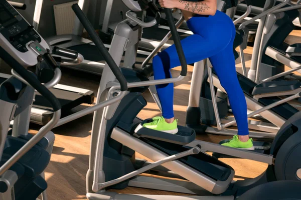 タイトなレギンスの女性の足は楕円形のトレーナーに従事している ジムでの心臓トレーニング — ストック写真