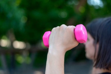 Kadınların elinde pembe dambıl. Açık hava fitness. Spor aletleri. Kapat.
