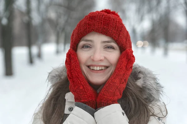 冬の瞬間を楽しむ赤い帽子の幸せな女の子のクローズアップ肖像画 雪に覆われた公園の背景に幸せな若い女性 — ストック写真
