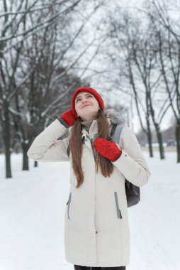 Güzel genç bir kadın kış ormanındaki karlı ağaçların arasında dikiliyor ve bakıyor. Dikey çerçeve