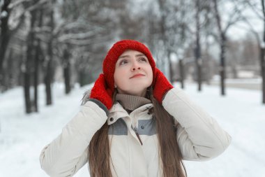 Kışın güzel bir kadın. Kar kaplı parkta kırmızı şapka ve eldivenleri düzelten bir kızın portresi.