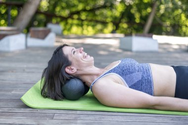Neşeli atletik kız yoga minderinde yatıyor ve miyofasyal toplarla boyun masajı yapıyor. Boyun kaslarını MFR pateniyle dizler..