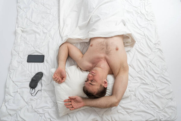 Portrait of young fast-sleeping man, top view. Sound sleep. Guy sleeps on white cotton bed linen