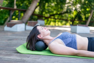 Atletik kız yoga minderine uzanıp boyun masajı yapıyor. Boyun kaslarını MFR pateniyle dizler..