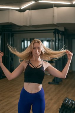 Spor salonundaki kendine güvenen atletik kadının portresi. Sarışın kız antrenmandan önce saçını düzleştirir.