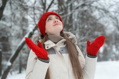 Parkta parlak şapkalı ve eldivenli genç bir kadının kış portresi. Noel arifesi. Kollarını açıp mucizeyi bekliyor.