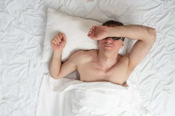 stock image Man sleeps soundly in bed, putting his hand on face. Portrait of sleeping guy top view