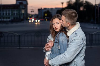 Guy hugs his beloved on evening city background.