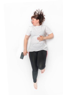 Portrait of plus size woman in sportswear lies and looks away on white background. Model with curvy figure. Top view.