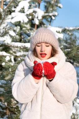 Beautiful young girl holding snow in mittens. Winter portrait in forest. Vertical frame.