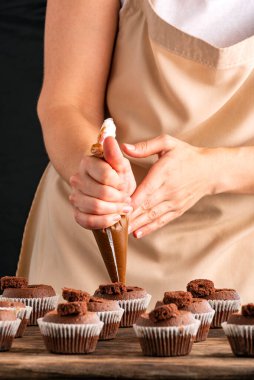 Pastry-cook hand prepare chocolate cupcakes. Vertical frame. Woman decorates muffins with cocoa cream in her kitchen