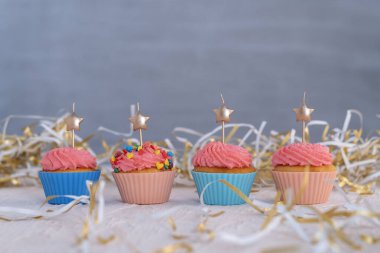 Holiday cupcake decorated with pink buttercream frosting and hearts. Muffins are decorated with star-shaped candles