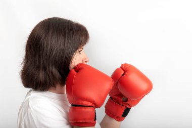 Portrait of young female boxer in red gloves on white background. Struggle for womens rights, feminism. Side view.