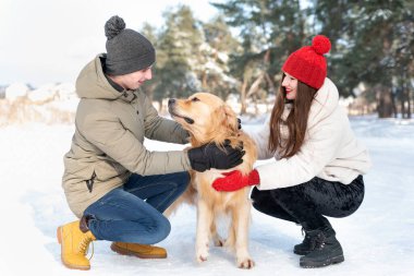 Portrait of young family with Golden retriever in winter forest. Walking the dog.