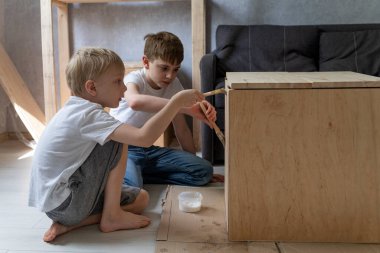 Children help renovate the wooden cabinet. Two caucasian boys paint the table with brushes. Restoring furniture