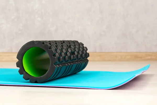 Black foam roller for self-massage on blue yoga mat. Equipment for myofascial release. Fitness Equipment. Side view.