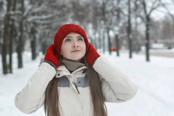 冬の美人 赤い帽子の少女の肖像画と雪に覆われた公園のミトン — ストック写真