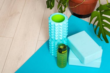 Foam roller for massage of muscle and fascia, gym blocks and a bottle of water. Sport equipment in home interior