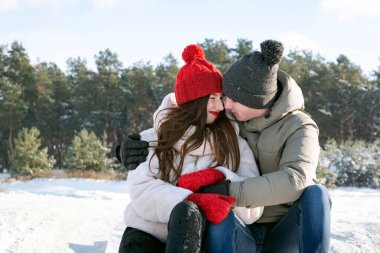 Teenagers sit and hug against the background of the winter forest. Date outdoors.