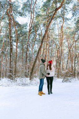 Young couple of lovers stands in the winter forest and looks at each other. People Outdoors. Vertical frame.